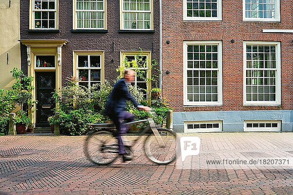 Motion blurred bicycle rider cyclist man on bicycle very popular means of transport in Netherlands in street with old houses of Delft  Netherlands
