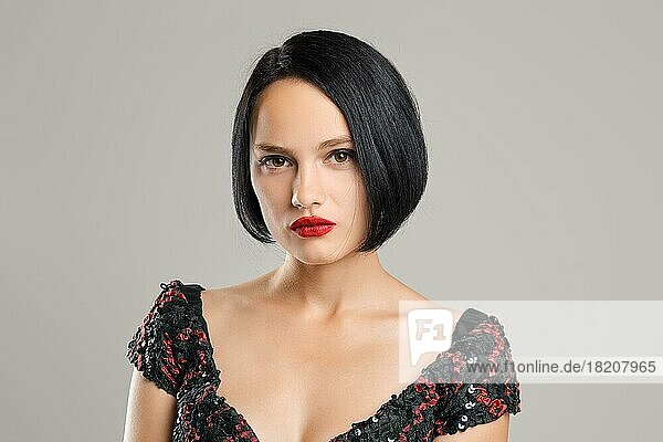 Seriöse Dame mit kurzen dunklen Haaren und roten Lippen posiert im Studio