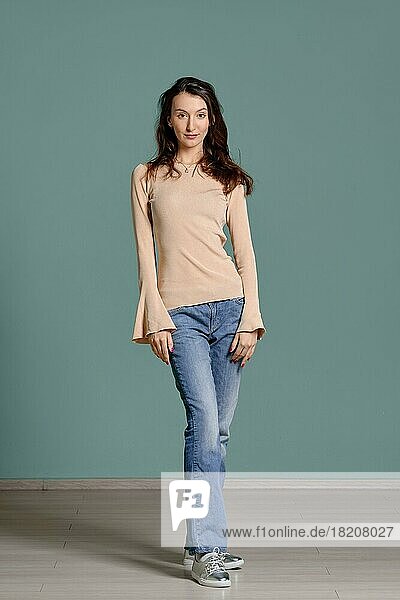 Full length portrait of trendy young woman in beige jersey longsleeve and straight blue jeans