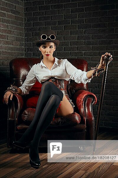 Porträt eines schönen Steampunk-Mädchens in Unterwäsche und Strümpfen  das in einem alten Sessel sitzt und sich auf einen Stock stützt