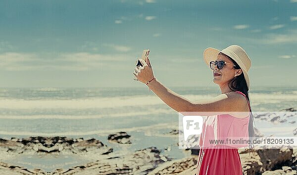 Junge Frau im Urlaub macht Fotos am Strand  Lächelndes Mädchen mit Hut macht Fotos am Strand. Strandurlaub Konzept. Mädchen mit Hut am Strand nehmen ein Selfie