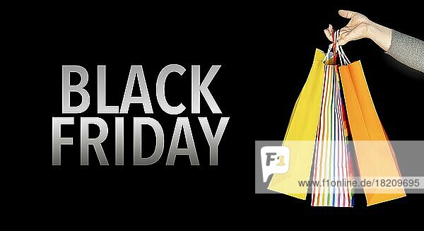 Black Friday kommerzielle Veranstaltung. Nahaufnahme einer Frauenhand  die bunte Einkaufstaschen vor schwarzem Hintergrund hält