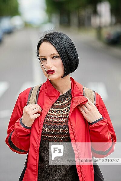 Closeup Porträt von niedlichen nachdenklich Mädchen in roter Jacke und Rucksack auf der Straße