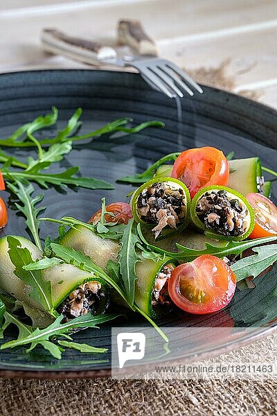 Gehackter Räucherlachs und schwarze Oliven  gerollt in Gurke  dekoriert mit Tomate und Rucola