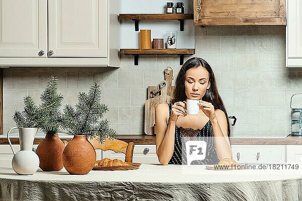 Verschlafene gemischtrassige Frau  die morgens in der Küche frischen Kaffee trinkt