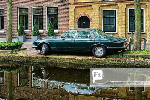 Altes schwarzes Retro-Auto am Kanaldamm in einer Straße von Delft mit Spiegelung. Delft  Niederlande  Europa