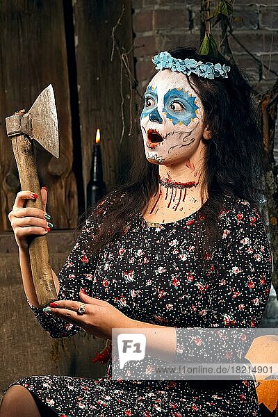 Junge Frau mit Axt und Zuckerschädel Make-up während Halloween. Gesichtsbemalung Kunst