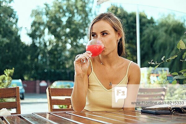 Schöne junge Frau trinkt kalte Erdbeerlimonade auf der Terrasse an einem heißen sonnigen Tag
