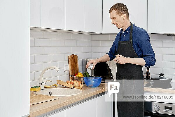 Mann mittleren Alters schüttet Salz in die Küche und macht ein Omelett