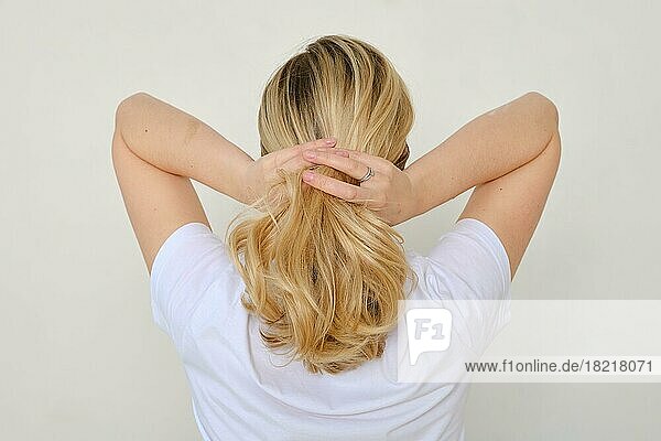 Rückansicht einer Frau  die ihre Haare frisiert und ein Band um ihr Haar bindet