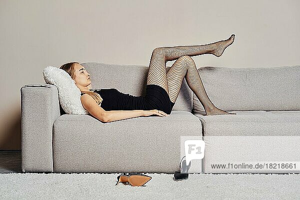 Eine müde Frau  die ihren müden Beinen Ruhe gönnt  lässt ihre Schuhe auf den Boden fallen und legt sich auf das Sofa