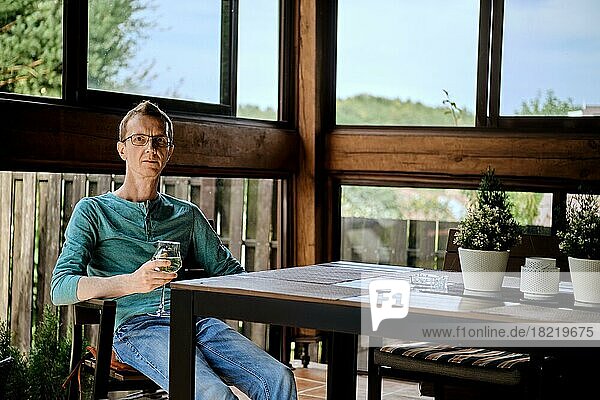 Ein Mann mittleren Alters ruht sich mit einem Glas Wein auf der Veranda aus
