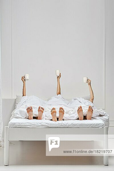 Drei weibliche Hände im Bett  die eine Tasse frischen Kaffee über der Decke halten