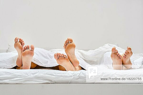 Drei Paar weibliche Fußsohlen  die unter der Decke hervorkommen. Konzept für einen faulen Morgen