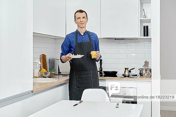 Ein Mann mittleren Alters bringt einen Teller mit gesundem Essen an den Küchentisch