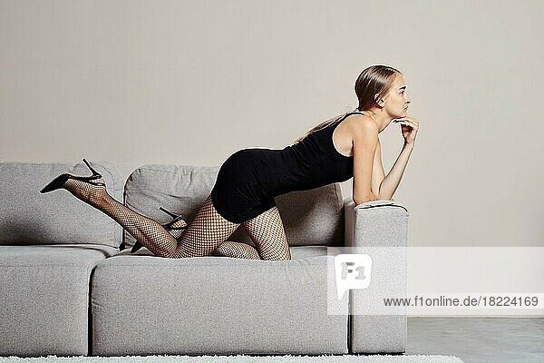 Junge Frau im kleinen schwarzen Kleid stützt sich auf ihre Knie und Ellbogen auf dem Sofa ab