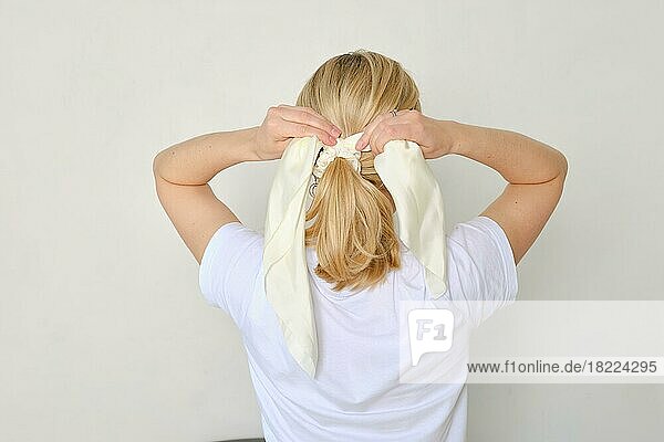 Rückansicht einer Frau  die ihre Haare frisiert und ein Band um ihr Haar bindet