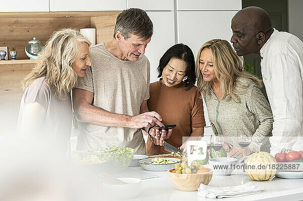 Diverse group of middle-aged friends checking a recipe while cooking