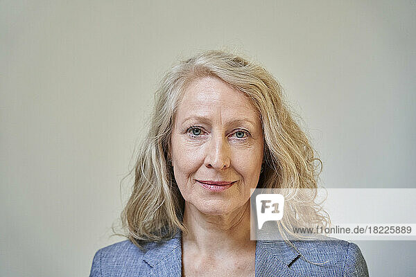 Senior blonde woman looking at the camera while standing against white background