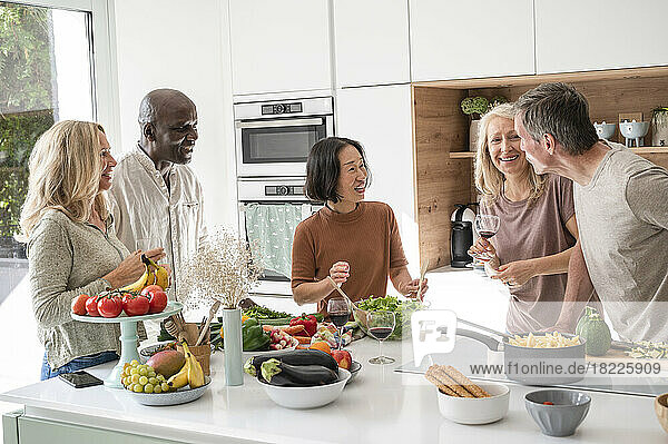 Group of diverse middle-aged friends getting together for dinner chatting in kitchen while cooking