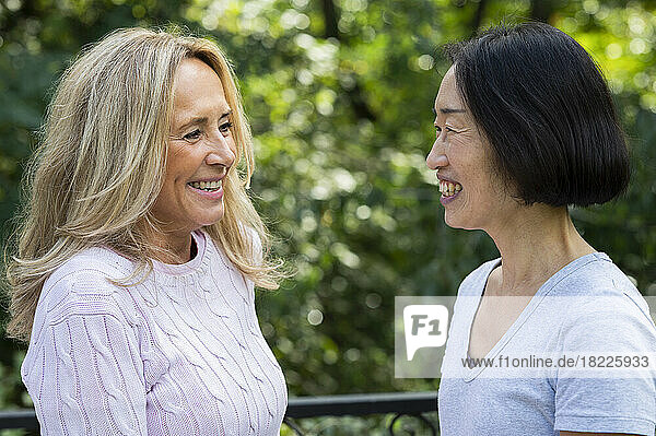 Side view shot of senior Asian-American woman and her friend smiling at each other while standing outdoors