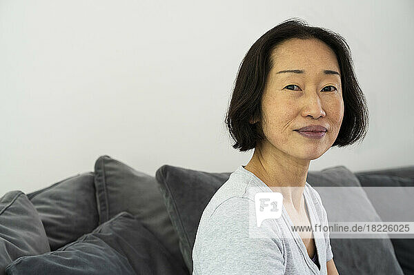 Portrait of Asian-American senior woman looking at camera and sitting in living room
