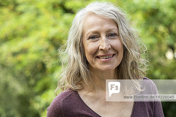 Portrait of middle-aged lady looking at camera while sitting outdoors in backyard