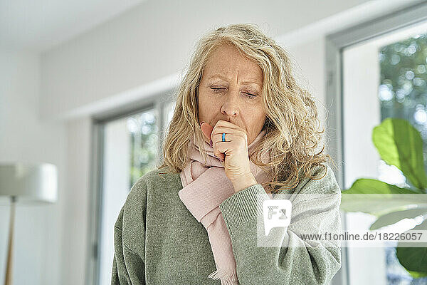 Senior woman sitting indoors while coughing