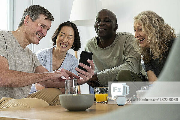 Middle-aged man showing a photo on his phone to his group of diverse friends indoors