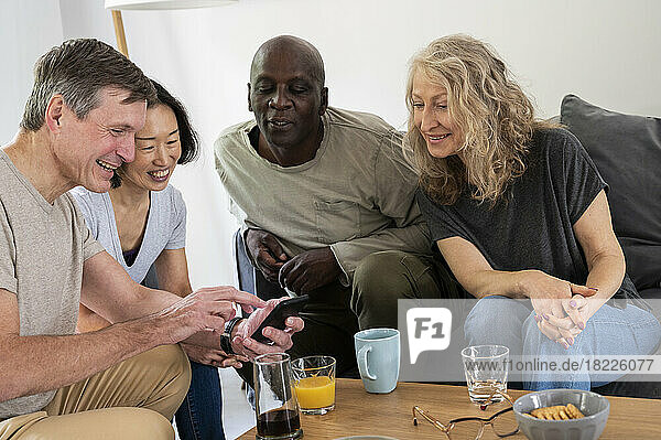 Fun diverse group of middle-aged friends looking at photos on cell phone at home