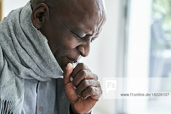 Senior African-American man wearing a scarf and coughing in his hand