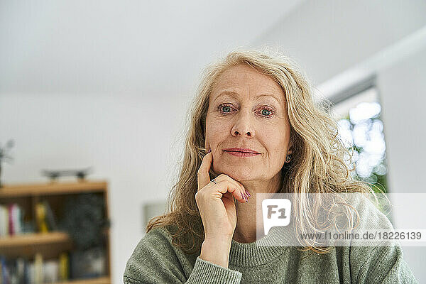 Thoughtful senior woman with hand on chin sitting in dining room