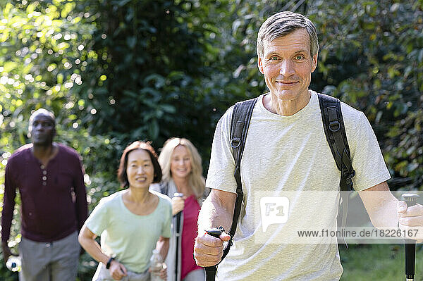 Handsome middle-aged man with hiking poles and backpack hiking in the local backroads with his diverse group of friends
