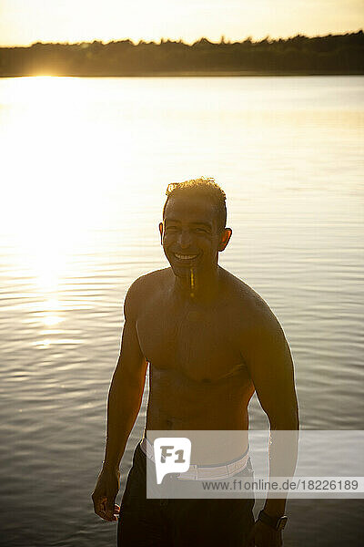 Glücklicher Mann ohne Hemd am See bei Sonnenuntergang