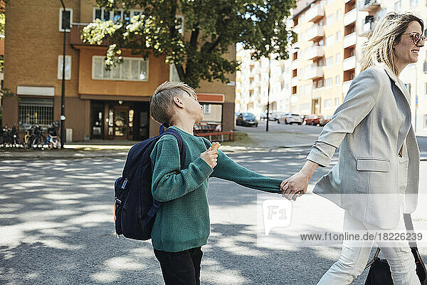 Side view of woman taking stubborn son to school while walking on street