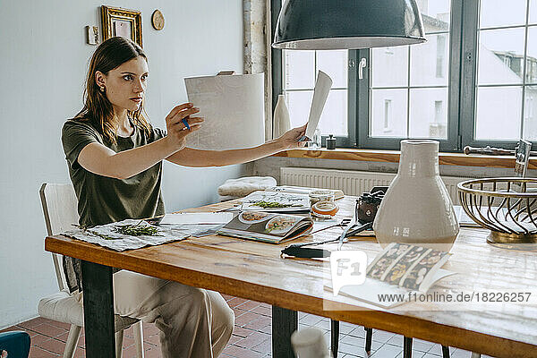 Konzentrierte weibliche Foodstylistin  die am Tisch sitzend im Studio Fotos vergleicht