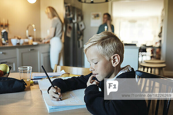 Nachdenklicher Junge macht Hausaufgaben in einem Buch  während er am Tisch sitzt