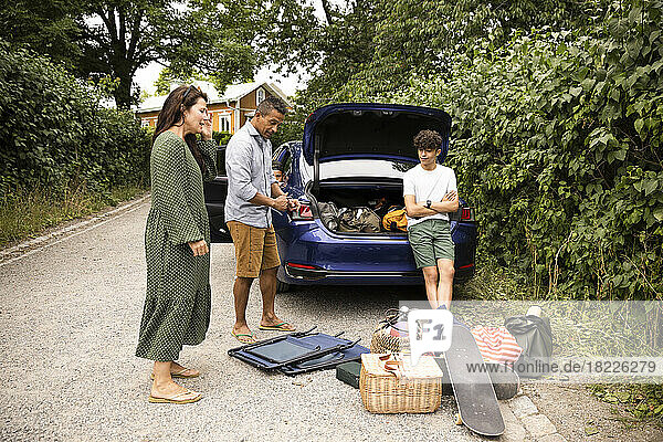 Familie diskutiert miteinander  während sie in der Nähe des Autos steht und sich Picknickzubehör ansieht