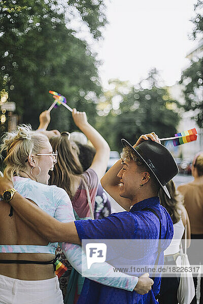 Glücklicher junger Mann  der einen Hut trägt  während er sich mit einer Freundin bei der Gay Pride Parade vergnügt