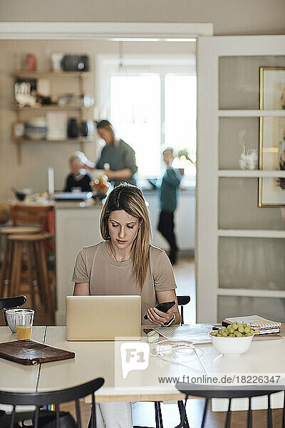 Geschäftsfrau hält Smartphone  während sie zu Hause am Laptop arbeitet