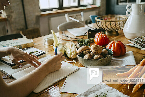 Hand einer Foodstylistin  die neben frischem Gemüse auf einem Tisch im Studio Tagebuch schreibt