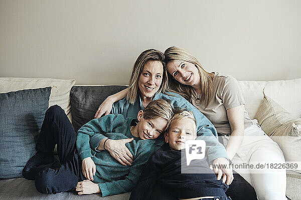 Porträt von lesbischen Müttern mit Söhnen  die zusammen auf dem Sofa zu Hause sitzen