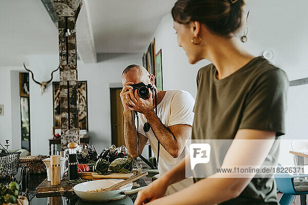 Männlicher Fotograf  der eine Köchin beim Kochen im Studio fotografiert