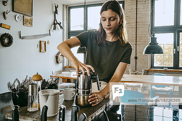 Eine Unternehmerin schraubt einen Wasserkocher an  während sie im Studio Kaffee zubereitet