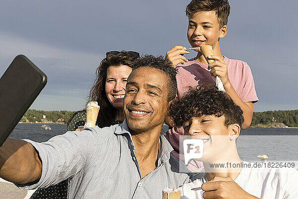 Glücklicher Mann  der ein Selfie mit seiner Familie über sein Smartphone macht  während er im Urlaub ein Eis isst