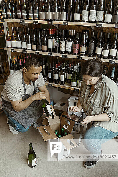 Männliche und weibliche Besitzer prüfen den Bestand an Flaschen  während sie in der Weinhandlung kauern