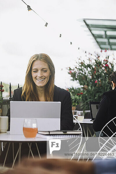 Glückliche weibliche Fachkraft sitzt mit Laptop im Café