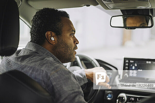 Männlicher Berufstätiger mit drahtlosen In-Ear-Kopfhörern beim Autofahren