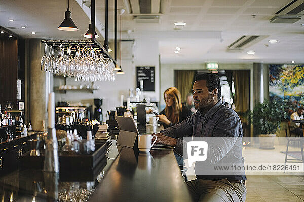Männlicher Freiberufler  der einen Laptop benutzt  während er an der Theke eines Restaurants sitzt