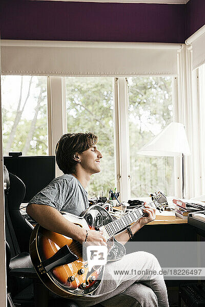 Junger Mann mit geschlossenen Augen spielt Gitarre  während er zu Hause sitzt